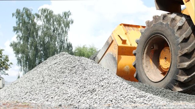 Large yellow tractor loader collects small gravel in the bucket, close-up, loader and small gravel