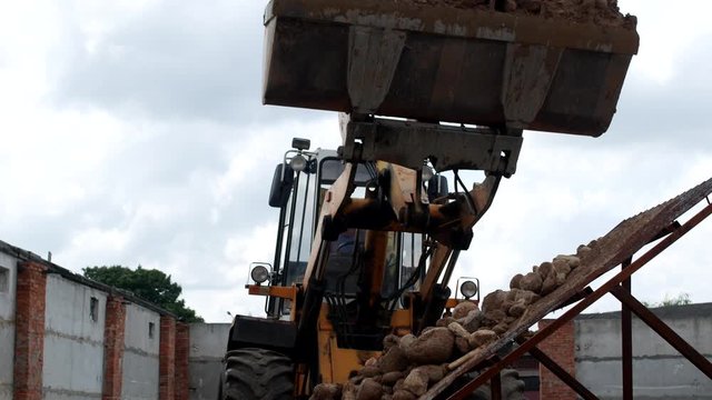 A large loader pours out ladle stones with sand on the seed drill to separate the sand from the stones, sower