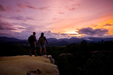 Silhouettes of two hikers with backpacks walking at sunset. Trekking and enjoying the sunset view