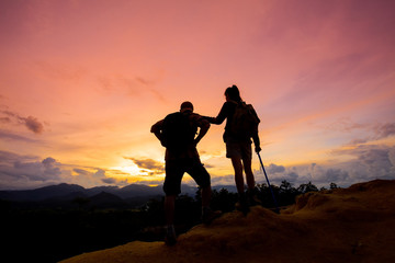 Hikers with backpacks standing on top of a mountain and enjoying sunrise