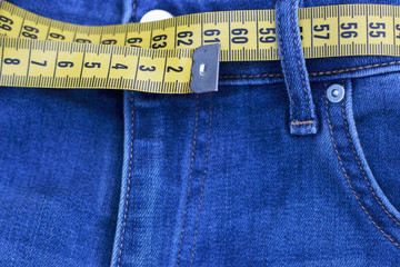 Centimeter tape, measuring as belt in jeans close-up, concept of losing weight. Healthy lifestyle.