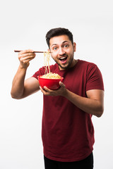 Indian/asian man eating hot noodles or ramen in a Red bowl with chopsticks