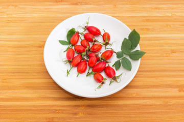 Red rose hips on white saucer on a wooden surface