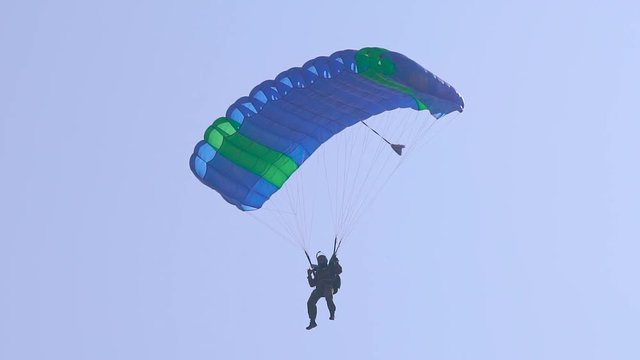 paraglider is flying in sky leading canopy by straps, view on sportsman from ground, tilt up