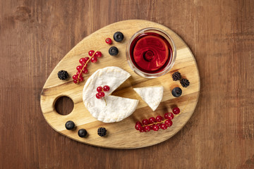 An overhead photo of Camembert cheese with a glass of red wine and fruits, on a dark rustic background with a place for text