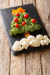 Christmas tree made of fresh vegetables broccoli, cauliflower, tomatoes, peppers close-up on the table. vertical