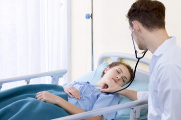 Medical professionals caucasian man examining patient with stethoscope in hospital, doctor using stethoscope to exam young woman sleeping.Close up.