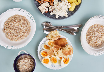 Light healthy Breakfast with oatmeal and coffee on a turquoise table. Hercules, nuts, fruit, boiled eggs, bread, coffee. Tableware. Healthy food. 