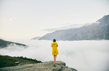 Obraz premium A young Girl in a yellow raincoat photographs the mountains. Georgia. Summer. August. Girl making a photo shoot of mountain. 
