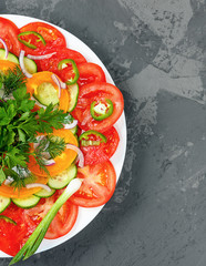 Salad of fresh vegetables on the white plate on the gray background. Top view