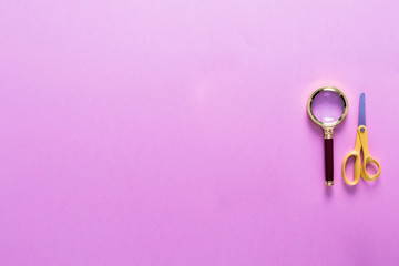 Top view over a magnificent glass and scissors on a pink background. Back to school concept. Office supplies flat lay