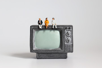 The old age miniature people sitting on the miniature television.