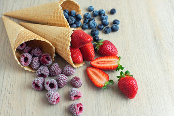 Strawberry, blueberry, raspberry in waffle cones on light wooden background