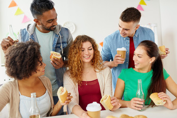 corporate, celebration and people concept - happy friends or team eating sandwiches with coffee and non-alcoholic drinks at office party