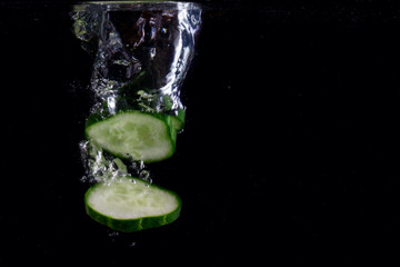 Fototapeta na wymiar pieces of cucumber go to the bottom on a dark background