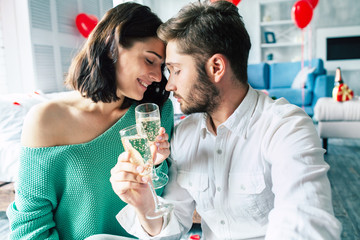 Beautiful stylish and cute romantic young couple are tender hugging each other, kissing and drinking champagne while celebrating some date or st. Valentines day at home.