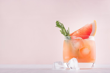 Cocktail d& 39 alcool de pamplemousse froid dans un verre embué avec une tranche de romarin et de pamplemousse sur fond rose pastel à la mode.
