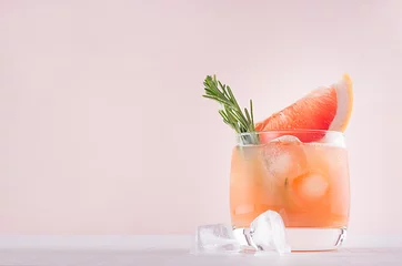 Keuken foto achterwand Cocktail Koude grapefruit alcohol cocktail in beneveld glas met rozemarijn en grapefruits segment op pastel mode roze achtergrond.