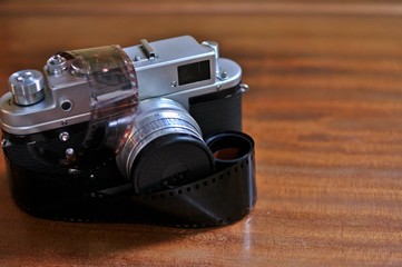 An old photo camera with retro style reel (roll) film 35 mm wrapped, on wooden background. Front...