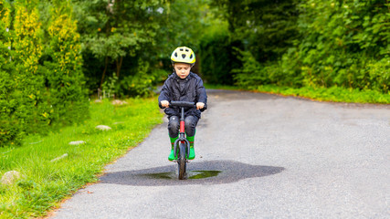 Little boy ride on balance bike in puddle. Childhood