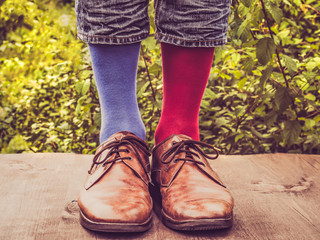 Men's legs in stylish shoes, bright, multi colored, variegated socks with Christmas and New Year's patterns on the wooden terrace on the background of green trees. Beauty, fashion, elegance