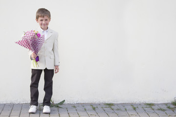 Boy first-grader in a smart suit with a bouquet of flowers