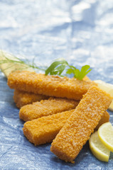 Breaded fried Fish fingers with lettuce and cherry red tomato with lemon slice on blue background with water splash 