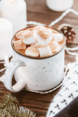 Hot cocoa with marshmallow in a white ceramic mug surrounded by winter things on a wooden table. The concept of cosy holidays and New Year.