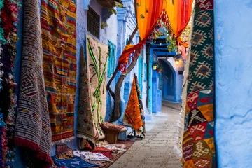 Zelfklevend Fotobehang Traditionele tapijten in de kleurrijke smalle straat van Chefchaouen in Marokko © Marko Rupena
