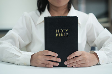 Close-up women christian read bible. Hands folded in prayer on a Holy Bible on white table.