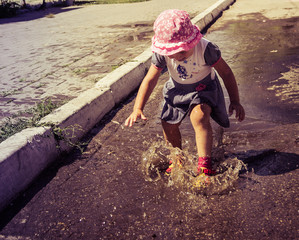 Cute baby sports and runs through the puddles on a summer sunny day