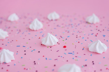 White meringues and colorful confetti on pink background.