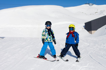 Two young children, siblings brothers, skiing in Austrian mountains on a sunny day