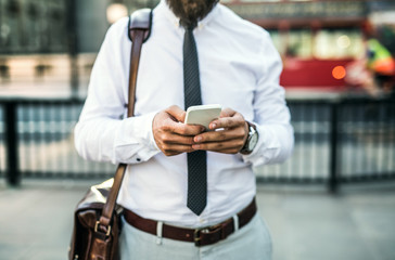 Unrecognizable businessman with smartphone standing on the street in city.