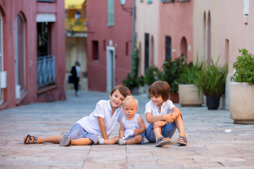 Fototapeta na wymiar Little baby boy, sitting on colorful street in the town of Villefrance, French Riviera with his brothers
