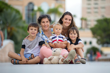 Grandmother with three grandchildren, sitting on the ground on the square in the city