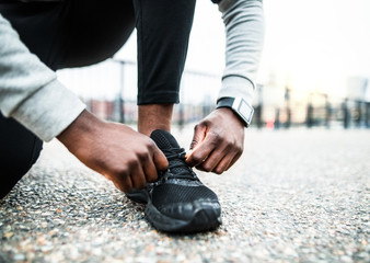 A close-up of a young sporty black man runner tying shoelaces outside in a city.
