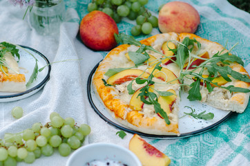 Pizza with chicken, peaches, cream cheese and arugula. Picnic on the grass with pizza, grapes, peaches and flowers