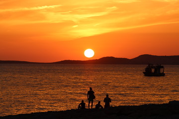 Fototapeta na wymiar Sunset with orange sky, big sun going down and boat silhouette