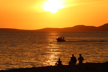 Naklejka na ściany i meble Ibiza sunset with boat and people silhouettes: golden light
