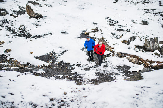 A Senior Couple Running Uphill In Snowy Winter Nature.