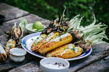 Tasty grilled corn cobs on old table with herb butter and lime on wooden table in the open air.