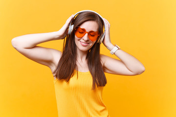 Portrait of calm smiling young woman in orange glasses listening music in headphones copy space...