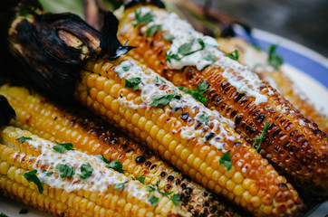 Tasty grilled corn cobs on old table with herb butter and lime on wooden table in the open air.