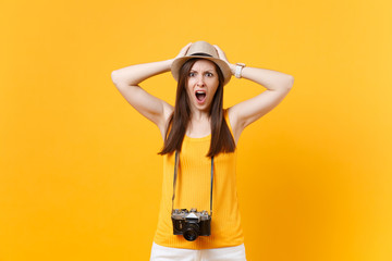 Shocked tourist woman in summer casual clothes, hat with retro vintage photo camera isolated on yellow orange background. Girl traveling abroad travel on weekends getaway. Air flight journey concept.