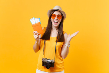 Expressive tourist woman in summer casual clothes, hat holding passport, tickets isolated on yellow orange background. Female traveling abroad to travel on weekends getaway. Air flight journey concept