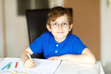 Naklejka na ściany i meble Cute little kid boy with glasses at home making homework, writing letters with colorful pens.