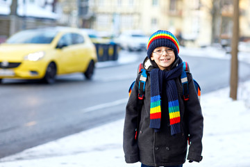 Fototapeta na wymiar Happy kid boy with backpack or satchel having fun with snow on way to school