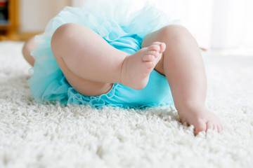 Closeup of legs and feet of baby girl on white background wearing turquoise tutu skirt.