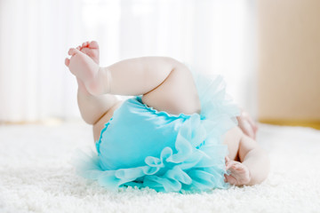 Obraz na płótnie Canvas Closeup of legs and feet of baby girl on white background wearing turquoise tutu skirt.